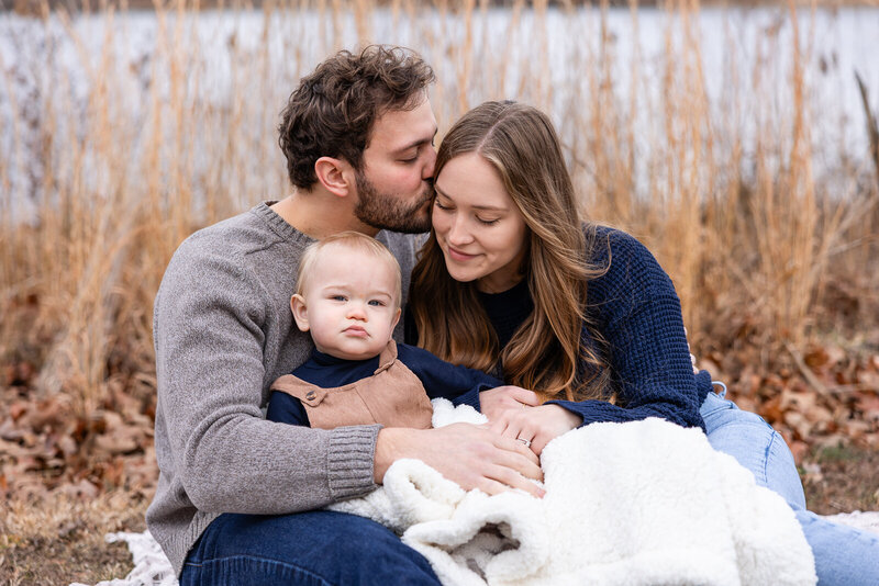 Family wrapped in a blanket cuddling outside in winter during a natural light family portrait session in Farmington, Missouri. 