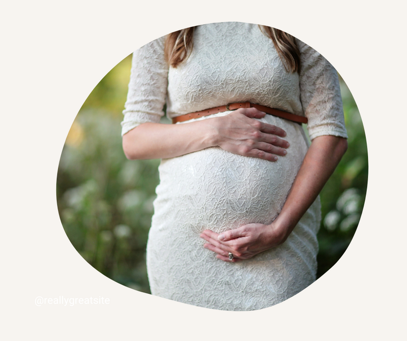 Pregnant woman in a lace dress holding her belly outdoors, representing pregnancy and postpartum therapy support. healing through Rooted Recovery eating disorder therapy at Rooted & Nourished Psychotherapy