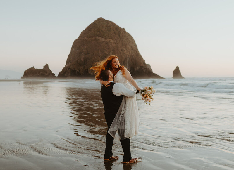 Elopement at cannon beach, oregon. Bride is holding a pink bouquet and couple is hugging on beach