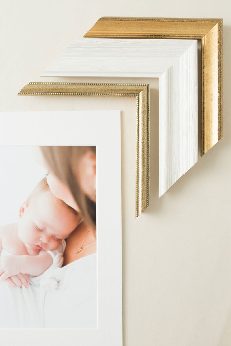 Eckstücke von goldenen und weißen Holzbilderrahmen gereiht an ein Foto von einer Mutter mit Ihrem Baby im Arm.