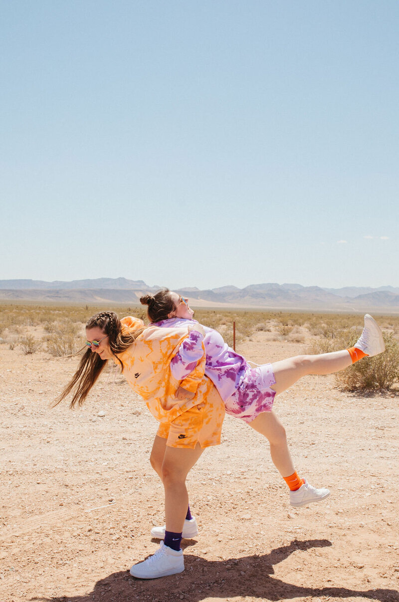 A girl picks up another girl on her back in the desert.