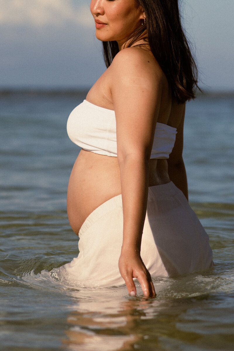 Woman posing in beach water for maternity photos in Oahu, Hawaii