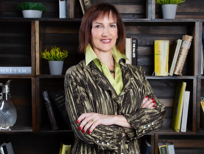 Business Headshot featuring Executive Coach Doctor Miluna Fausch standing in front of wood bookshelves with potted plants and books behind her
