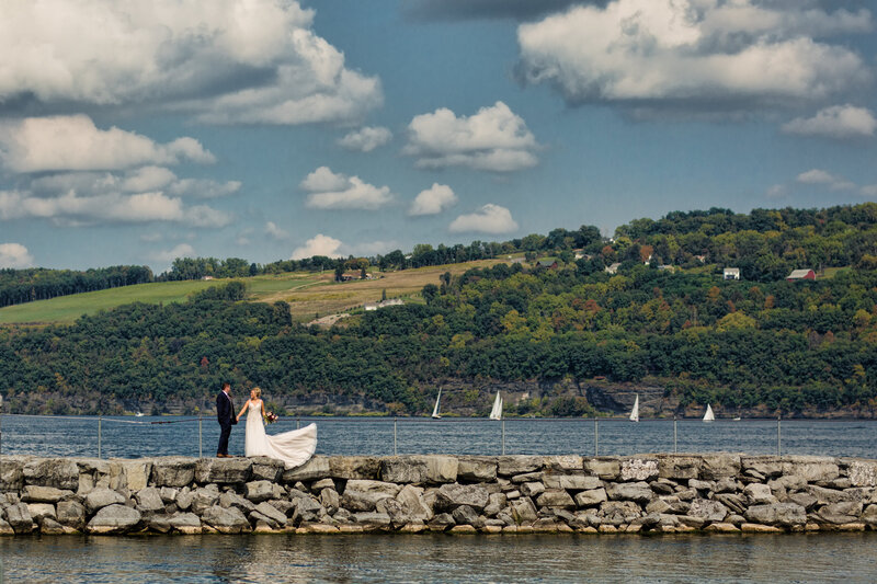 Bride and groom standing on a rock wall at Seneca Lake, capturing a serene destination wedding moment.