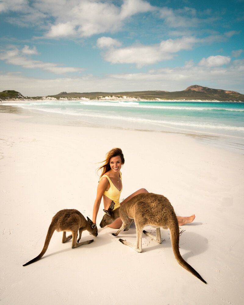 Jess of Jess Wandering in a yellow swimsuit sitting on a beach next to kangaroos
