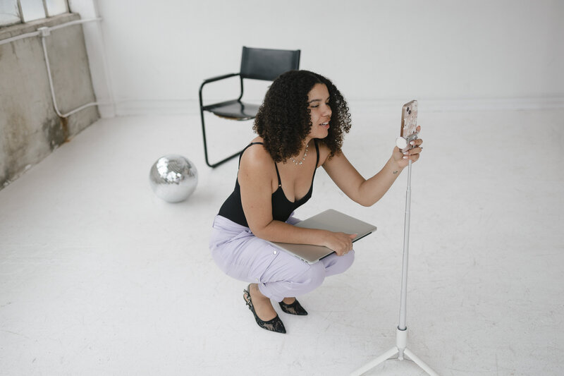 Photo of Catryce putting her phone on a tripod stand in purple pants with her laptop