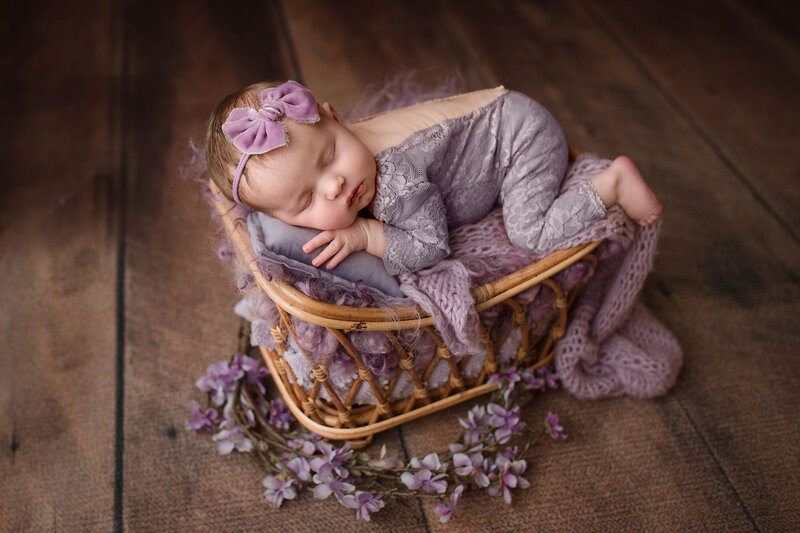 baby girl sleeping in a wicker basket dressed in lavender outfit