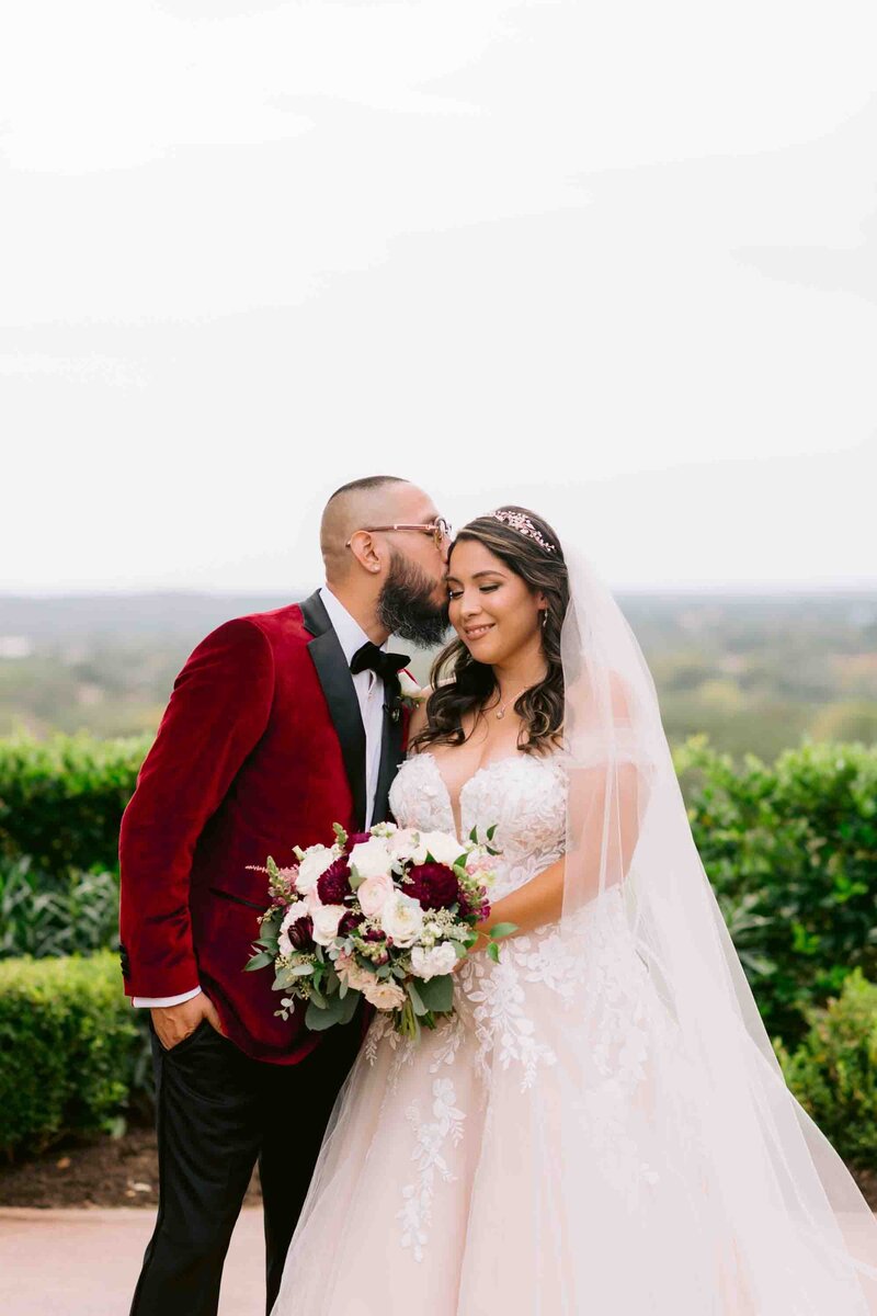 groom in red jacket kisses his bride