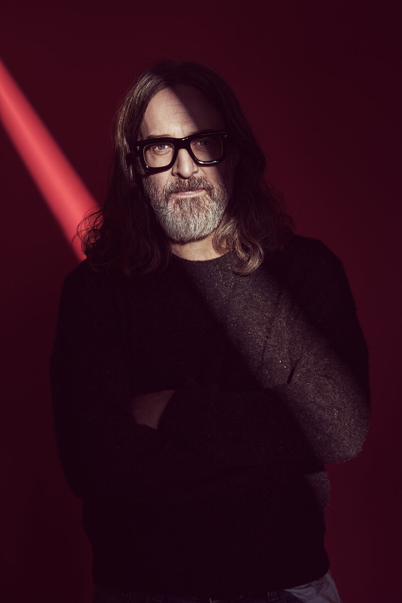 Studio portrait of Peter Stark with glasses, wearing a dark sweater, standing against a moody red background with dramatic lighting, captured by Ylva Erevall.