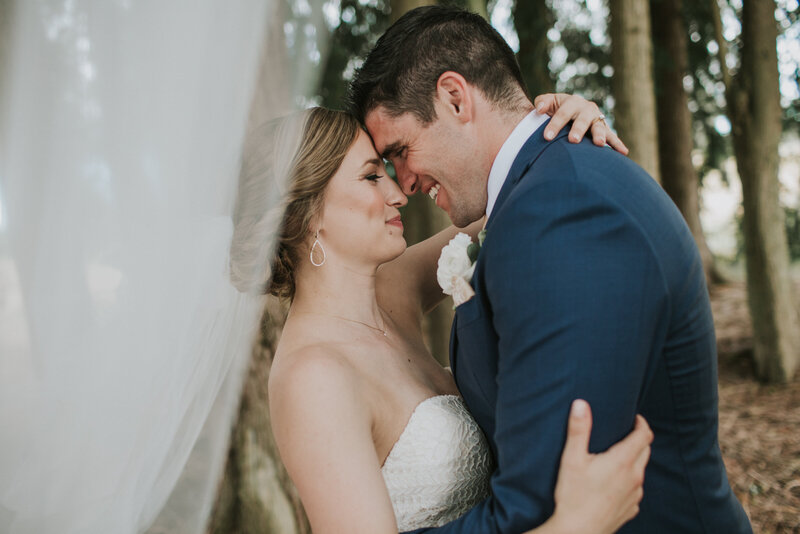 bride wearing a floor length veil in dramatic veil shot posing with her groom in the forest