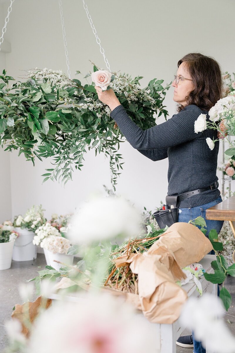 Columbus photographer captures florist brand photos with florist decorating a floral chandelier in an event space