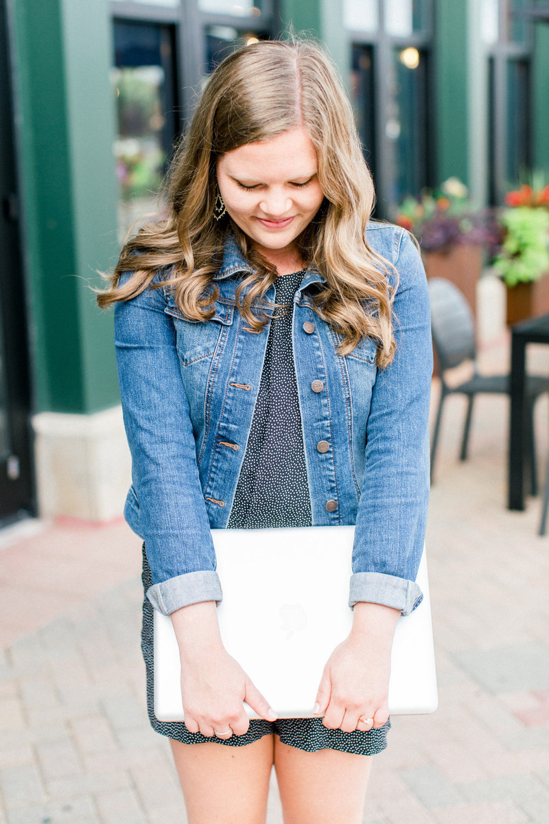 a woman in a jean jacket holding a laptop