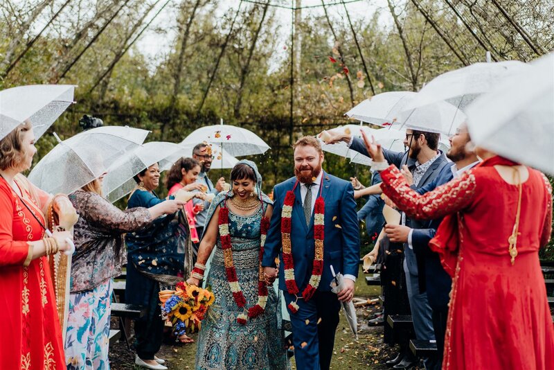 A bride and groom wearing traditional Indian wedding garb walking down the aisle at The Tree Church and Gardens in the Waikato