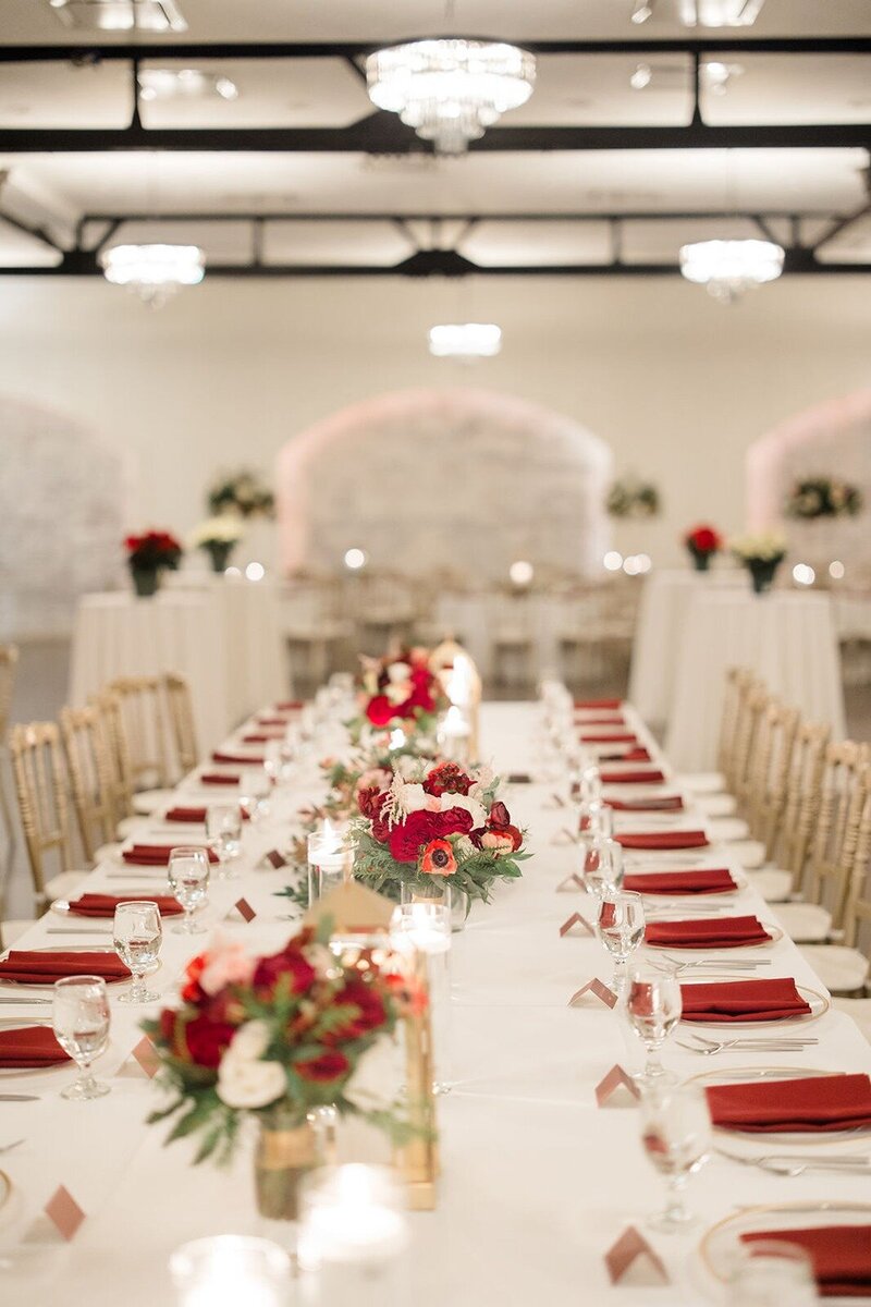 A luxury indoor space at Grbic Events in St. Louis is decorated with red napkins, glassware, candles, and red and white floral centerpieces.