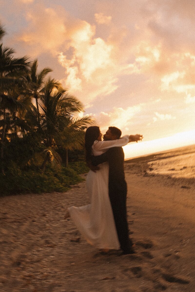 bridge and groom hugging on beach in hawaii