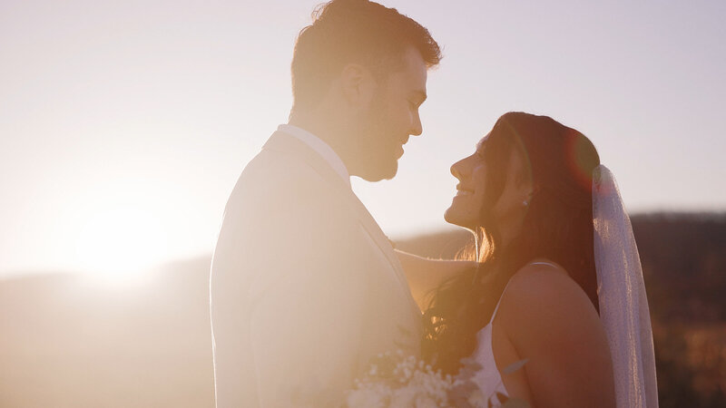 This wedding film frame grab from Films by Brian, a Williamsburg, VA-based destination wedding videographer, shows a beautiful bride holding her groom's hand at a Virginia marina,while looking into the camera.