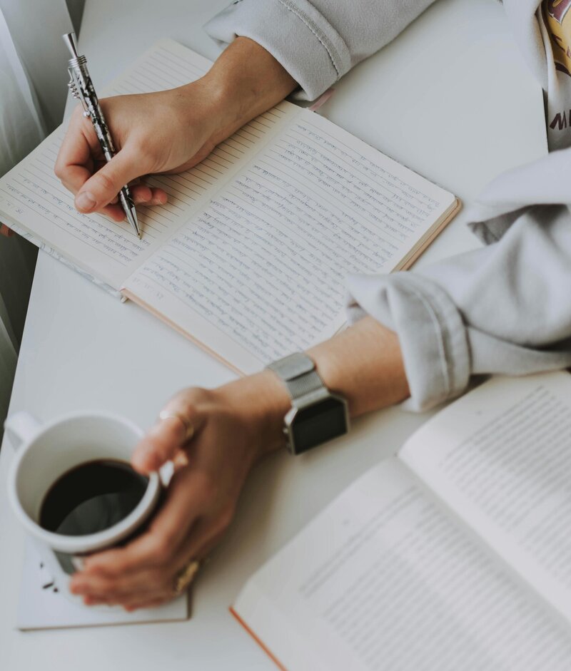 Woman journaling in a notebook with a cup of coffee in one hand