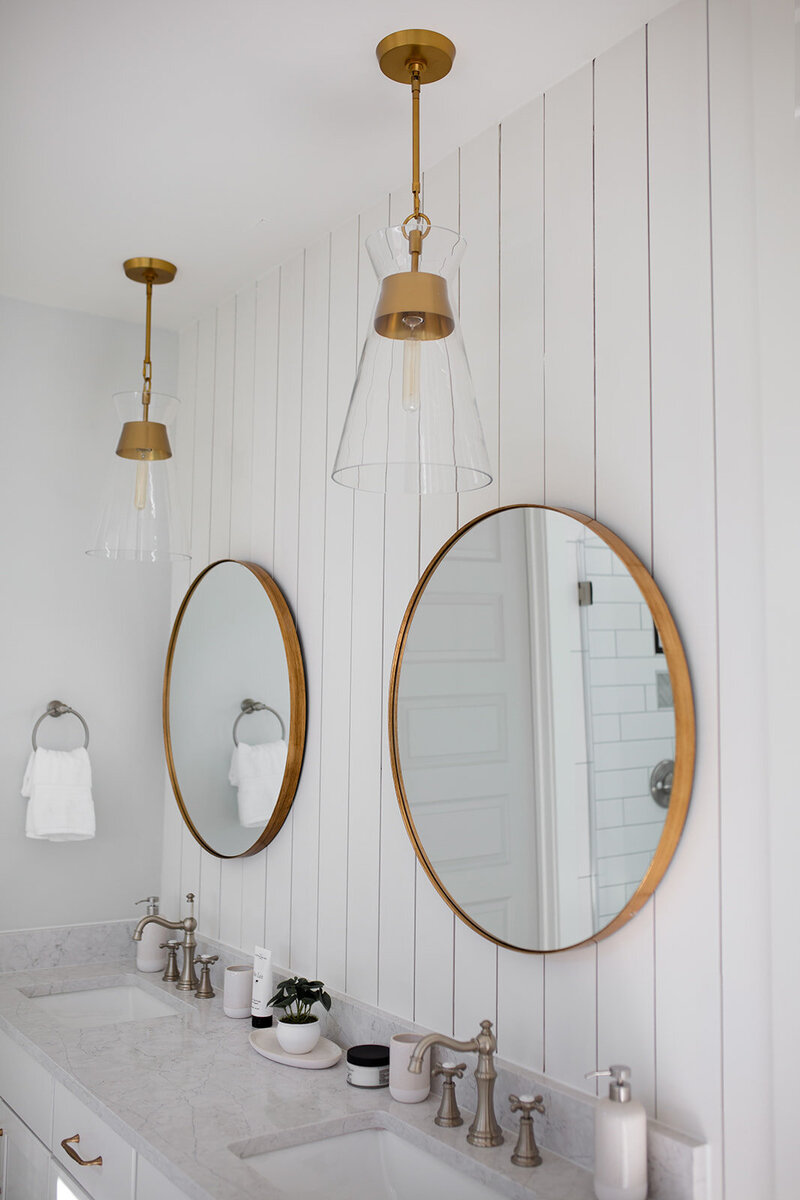 Bathroom with dual sink, all white. Round mirrors with bronze frame.