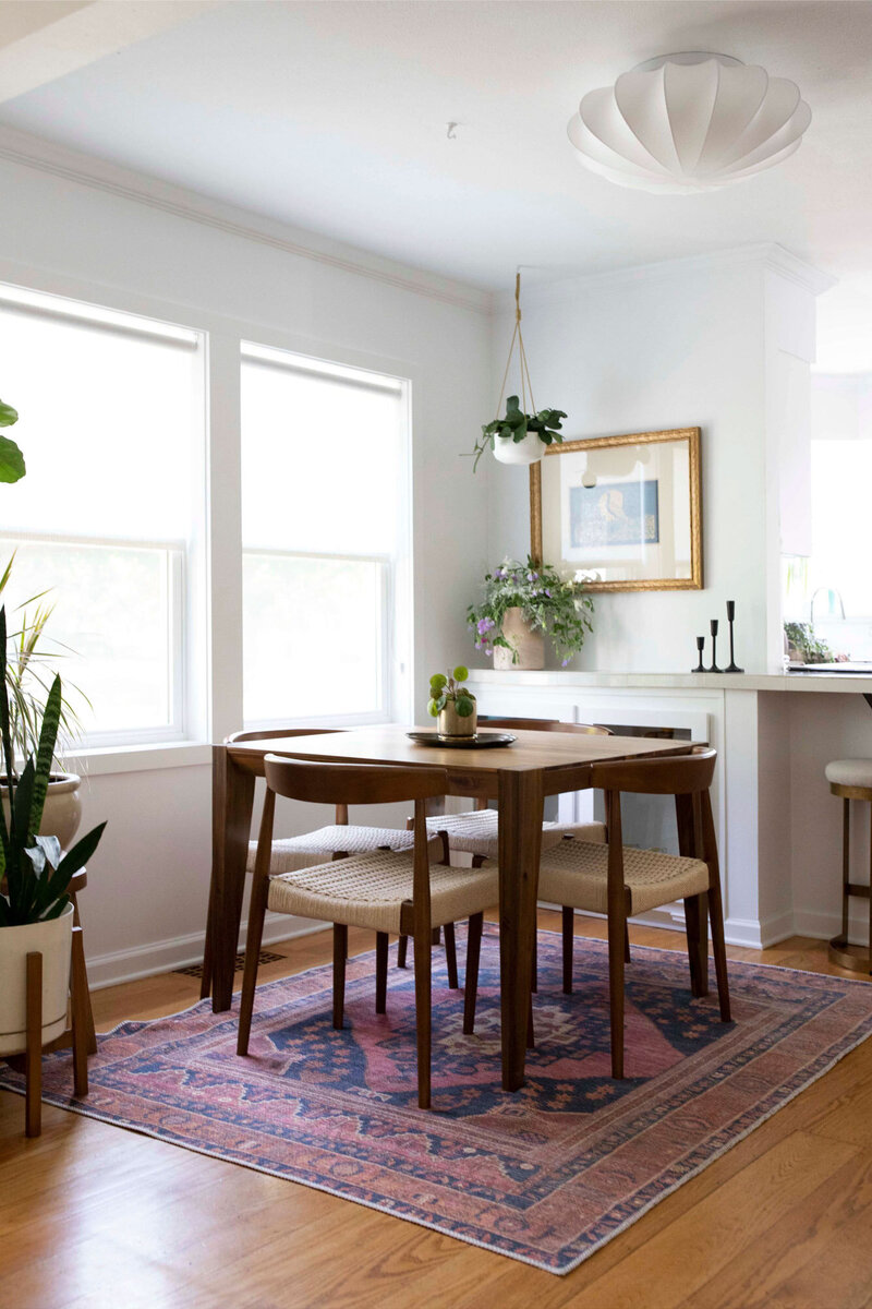 A dining room featuring a wooden table, patterned rug, and houseplants showcasing an art deco boho interior design.