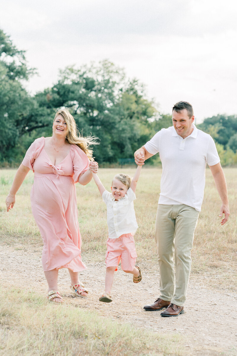 parents are making their toddler swing in between them and laugh while looking at the camera of their Cedar Park photographer.