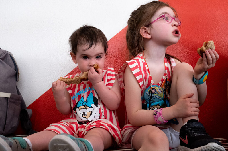 Two children sitting on the floor eating donuts.