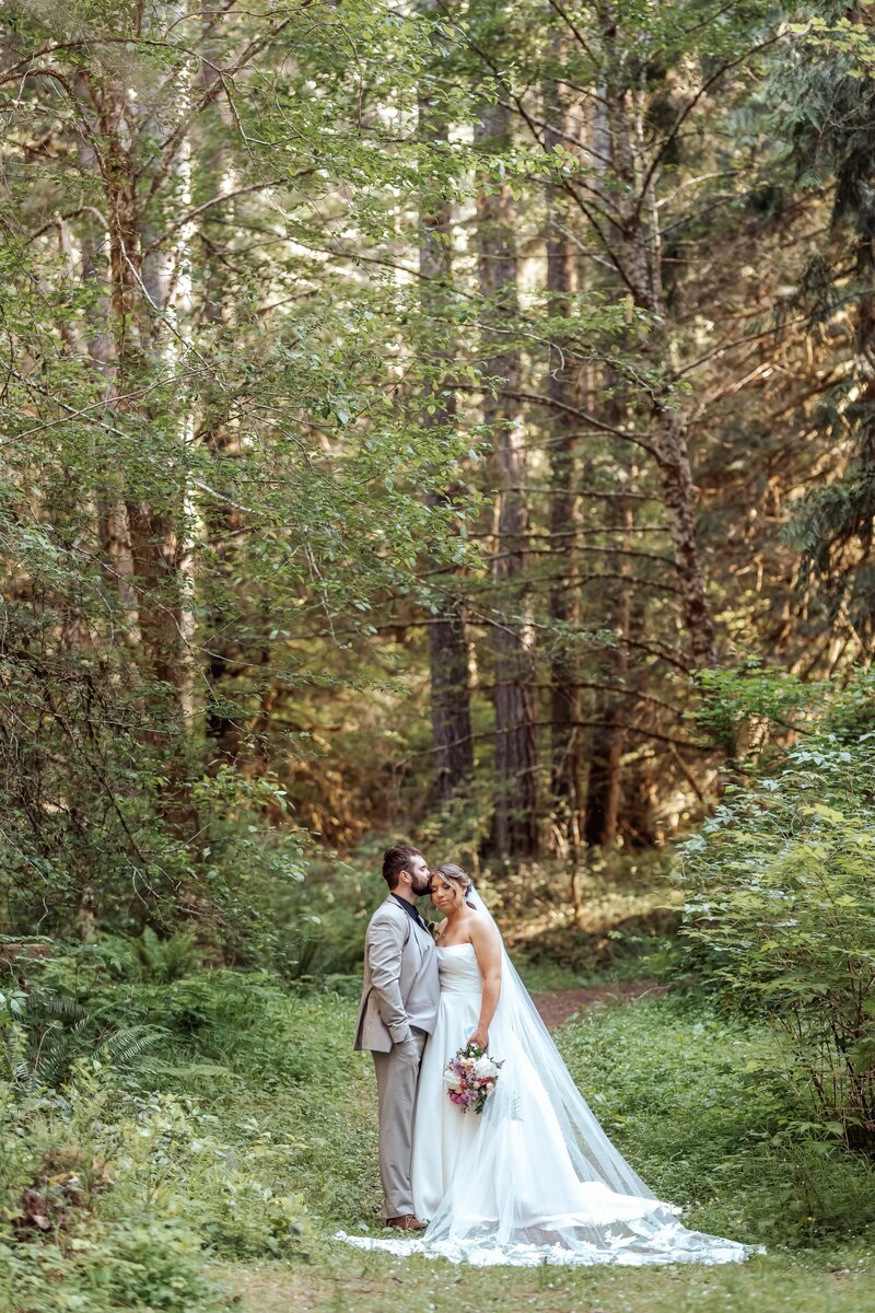 real bride and groom posing in forest with her custom lace bridal veil with vintage heirloom lace appliques