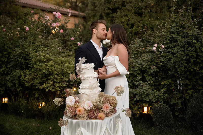 bride and groom share a kiss next to their wedding cake