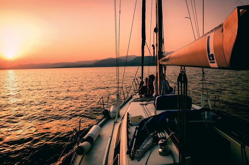 Segelboot auf dem Meer vor der Küste mit eingeholten Segel und 2 Personen vorne am Mast sitzend