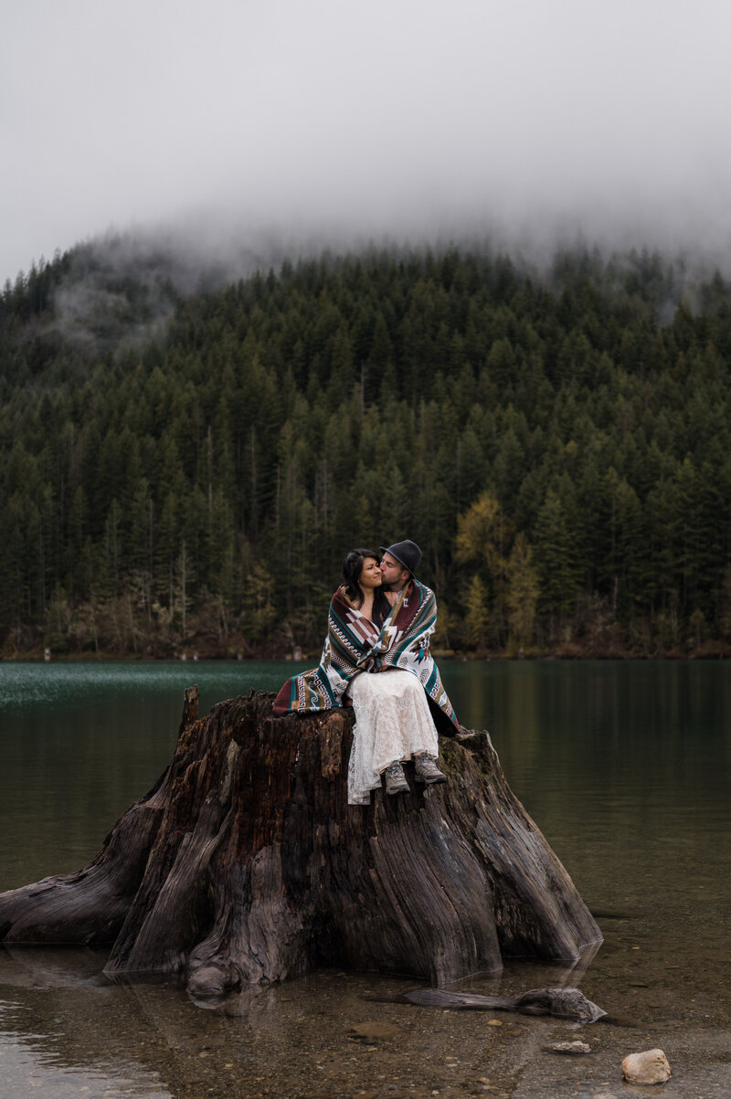 Couple at Rattlesnake Lake in Washington State snuggled up under a blanket during their moody spring elopement