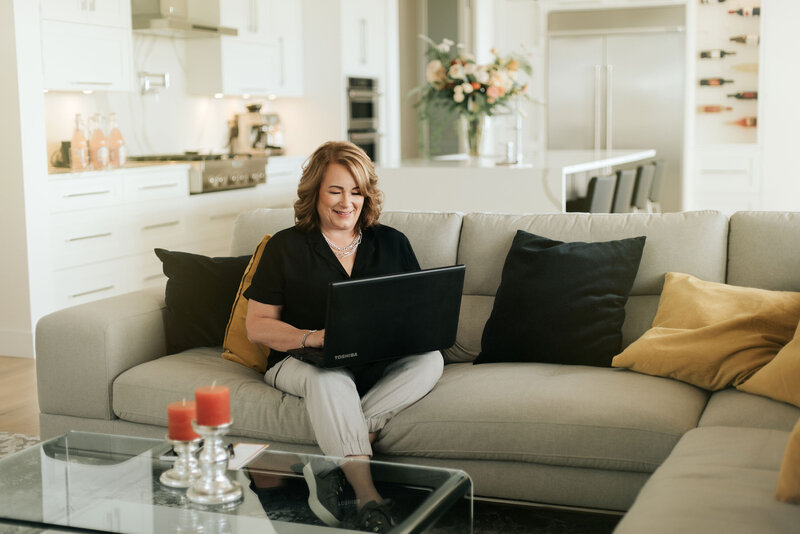 Joanne McCrone, a Port Moody real estate expert, working on her laptop in a stylish kitchen-living space.