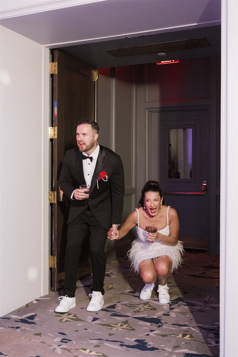 bride and groom walking getting a first look at their reception room in shock and awe with mouths gapped open holding hands with cocktails in their hands