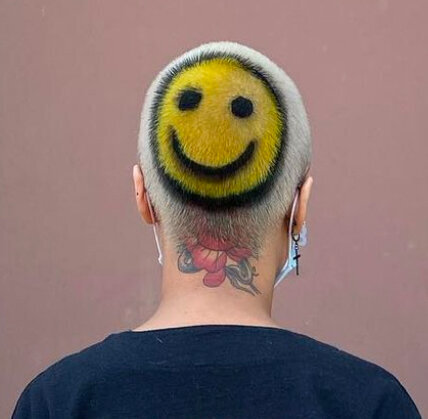 Image of hair salon client with short, bleached hair that has a yellow and black smiley face pattern dyed into the back of the head. 