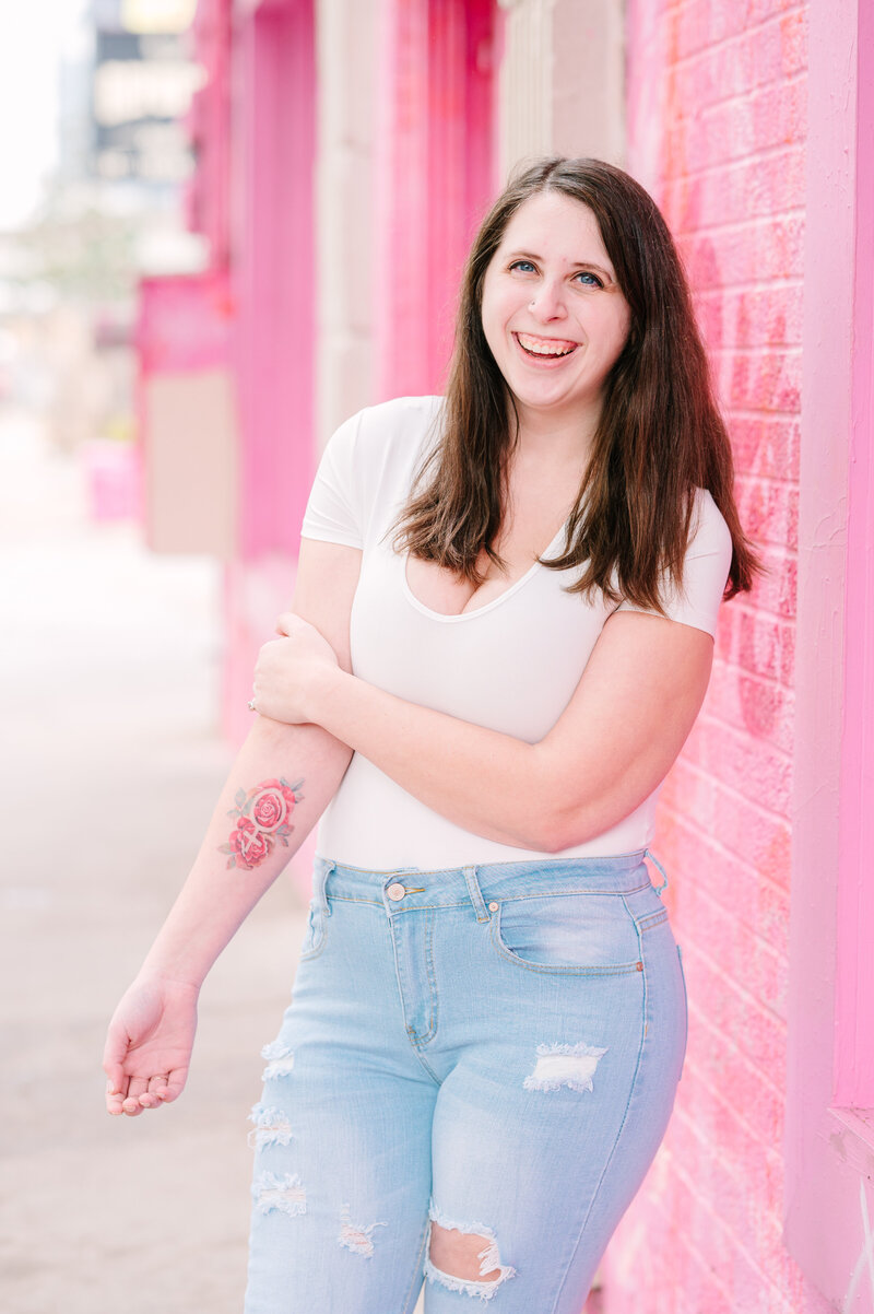 Cait Potter smiling in front of a pink brick wall
