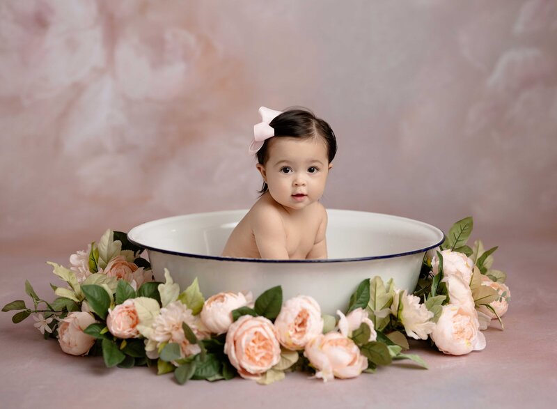 Baby girl sitting in a basin filled with milky water and pink flowers. Milestone baby photo taken at Atlanta Maternity photo studio in Woodstock GA.