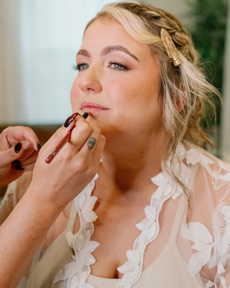 Close-up of a bride receiving a lip touch-up, wearing romantic bridal makeup with soft curls and glowing skin—glam by Artistry by Jessica.
