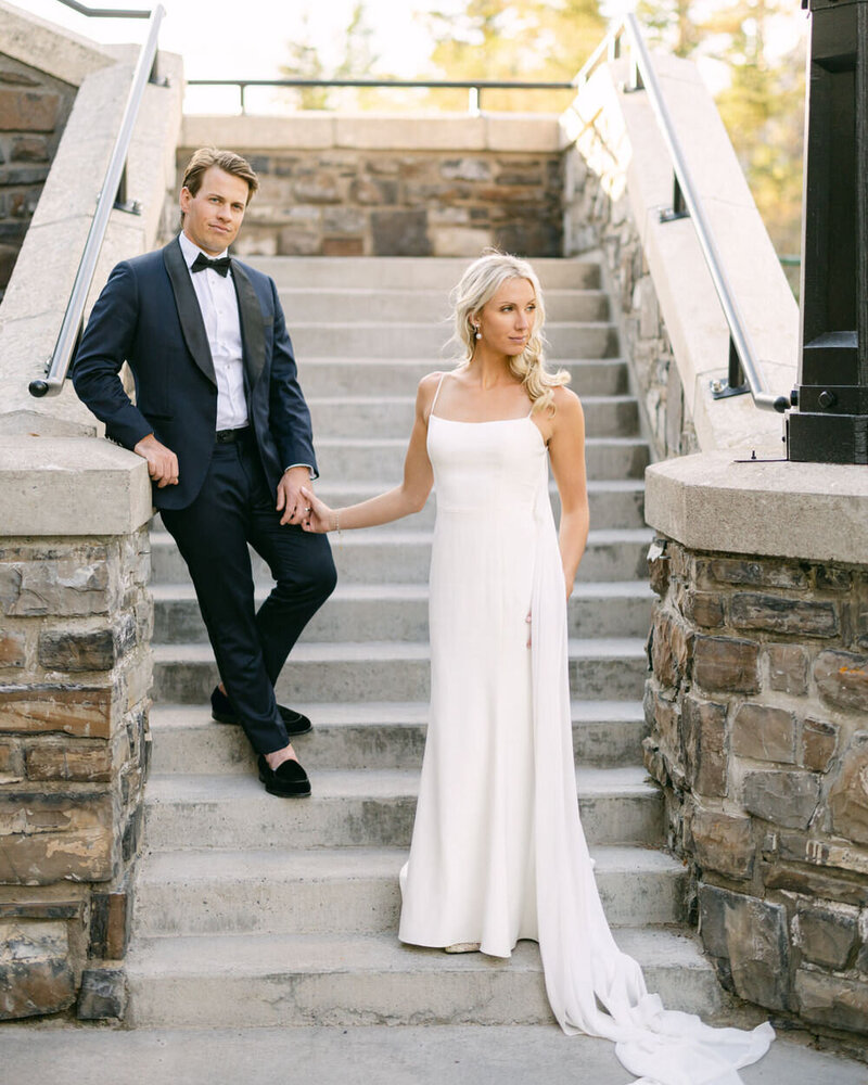 This romantic photograph captures a bride and groom holding hands on the iconic steps of the Banff Springs Hotel, leading up to the conservatory. Taken during the golden sunset hours, this intimate moment reflects the timeless elegance of their wedding day in one of Banff’s most cherished locations.