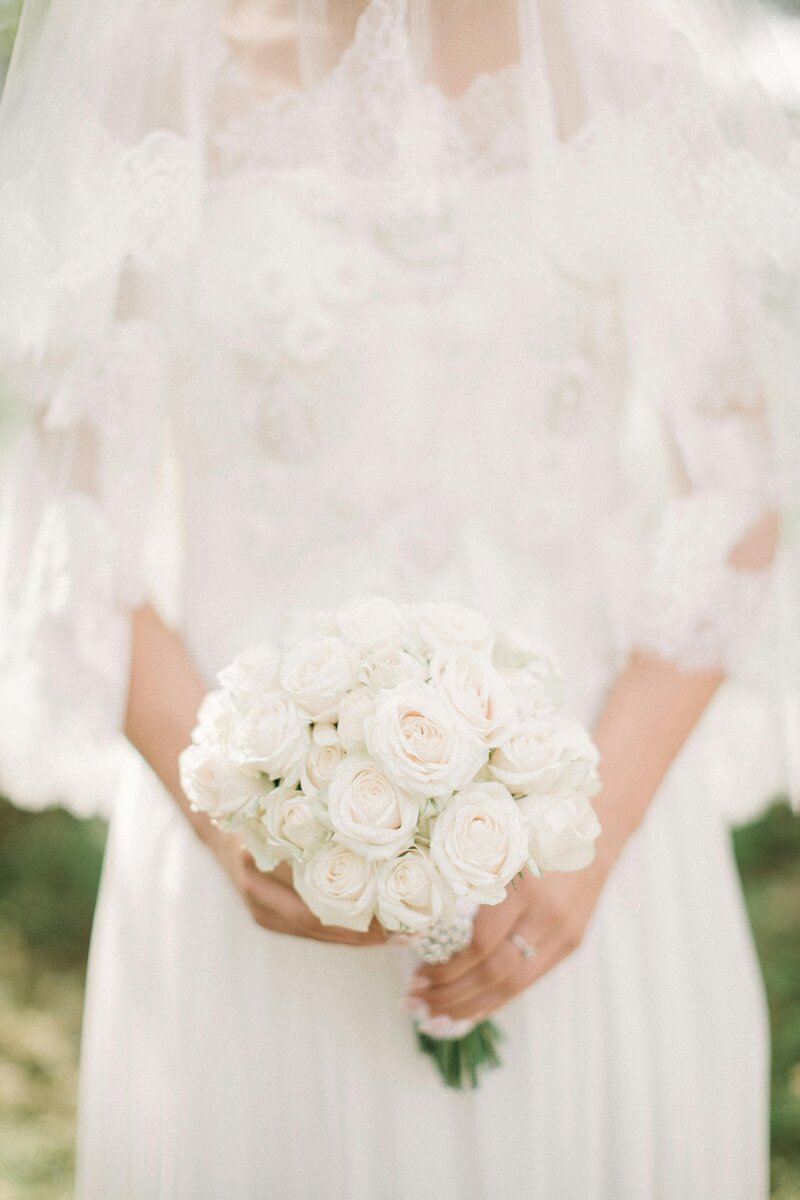 Bride holding an elegant bouquet of white roses in a lace wedding gown