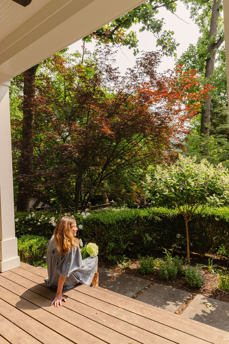 Woman sitting on wood plank porch looking out at backyard landscaping