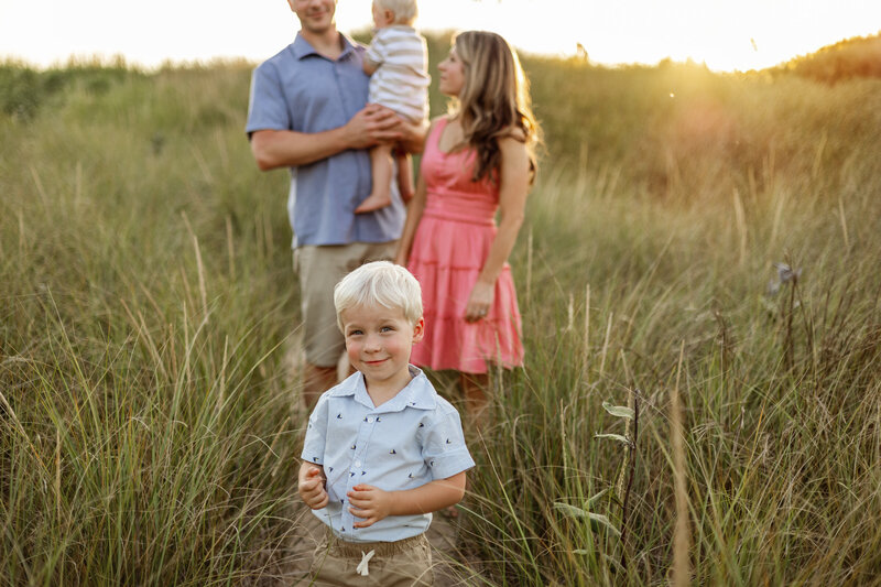 A family enjoying a relaxed outdoor photography session in Grand Rapids, Michigan, surrounded by tall golden grass. The warm sunlight highlights their genuine connection and love.