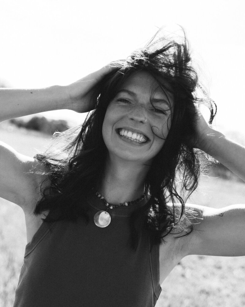 Black and white photo of a woman smiling while hair blows in the wind with arms up