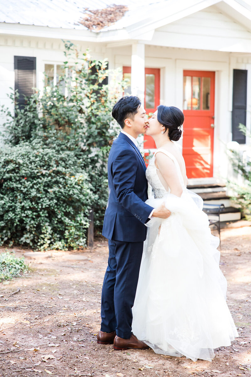 A bride and groom kiss in front of a small cottage at Payne Corley House