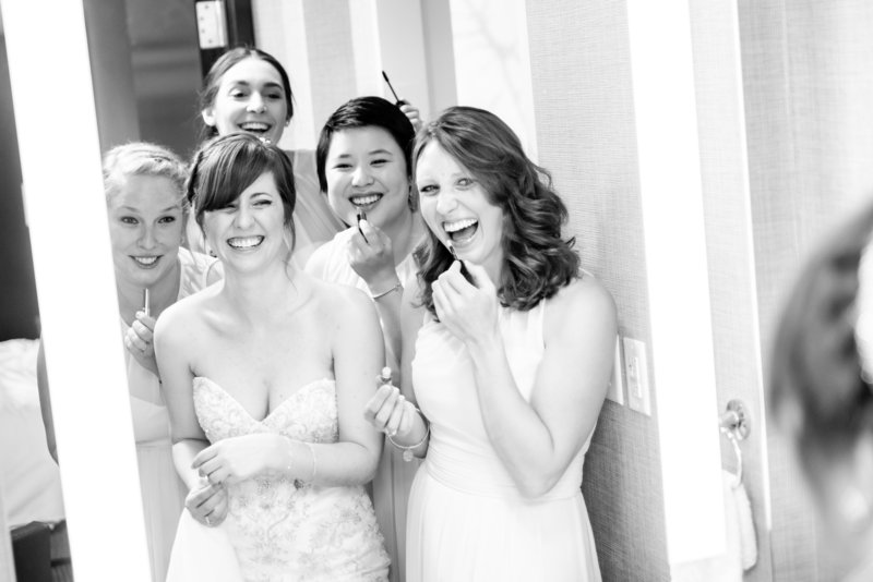 A bride and her bridesmaids put on their make-up while looking in the mirror