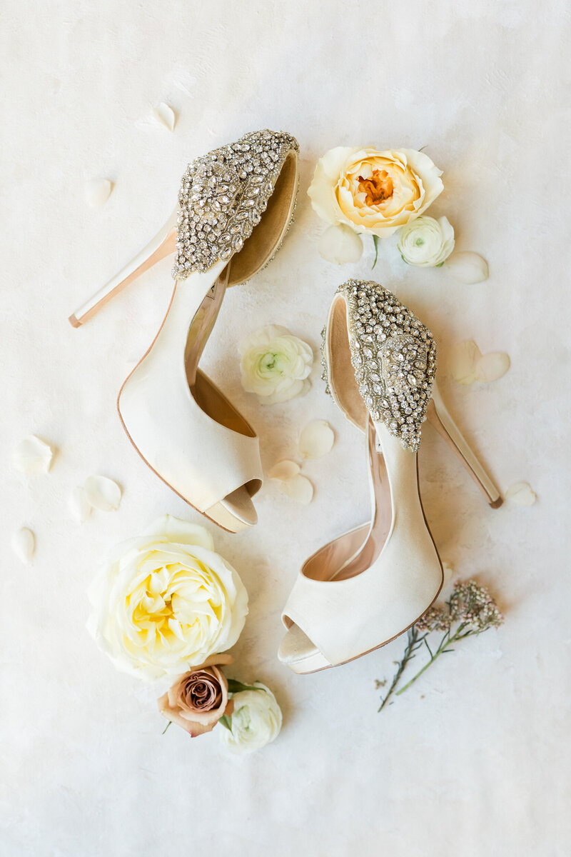 A flay lay image with Badgley Mischka shoes styled with flowers at a venue in Raleigh, NC, photographed by Raleigh wedding photographer Jenn Eddine..