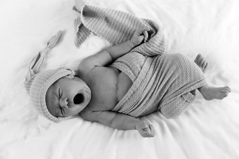 A yawning newborn swaddled in a soft blanket. Photographed by Sophie Louise for Nostalgia.