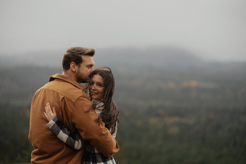 Couple embraces each other during their windy engagement session on Little Mountain on Vancouver Island