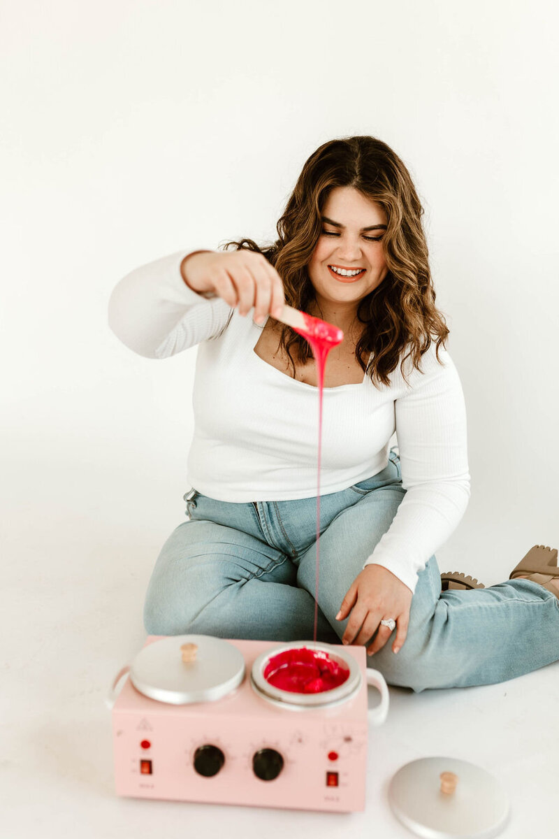 Licensed esthetician Macayla Hopper holding wax stick over wax warmer during body waxing prep in Hartselle studio