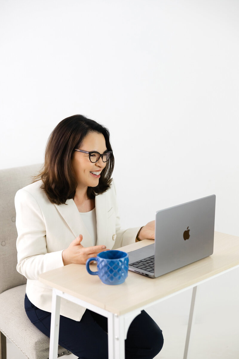 Leadership coach smiling during virtual session with coffee and laptop