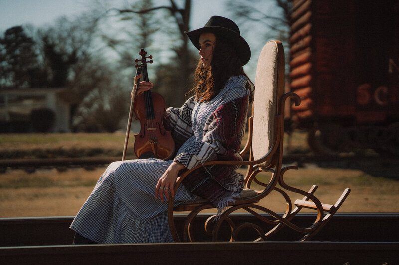 Appalachian violin player sits in a chair on train tracks posing for an album cover.