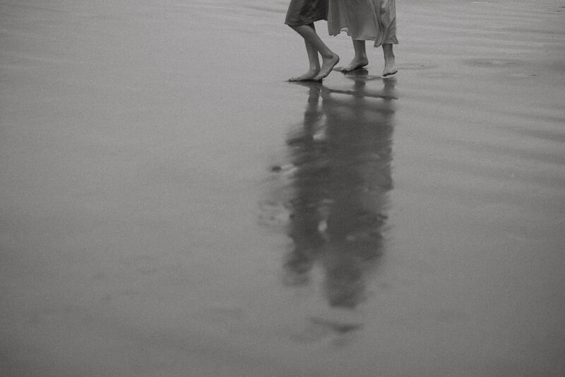 Couple walking barefoot along the rugged Oregon Coast on Hwy 101 near Yachats, Oregon, with crashing waves and rocky cliffs in the background.