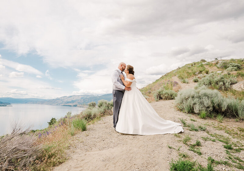 Romantic wedding portrait on top of a mountain in Penticton. the bride is wearing a long white wedding dress and the groom a gray suit